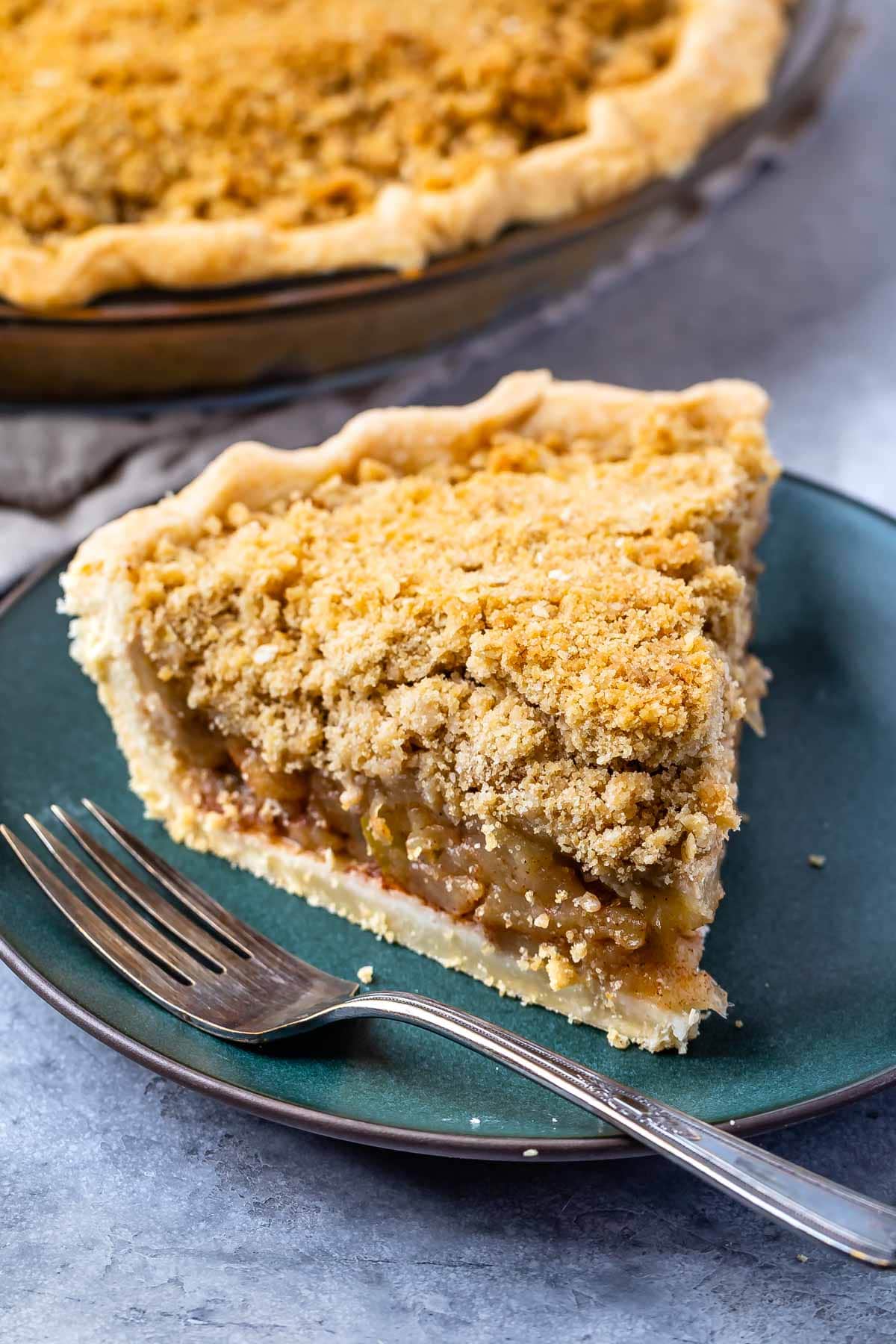 one slice of apple pie on a dark green plate with crumble topping