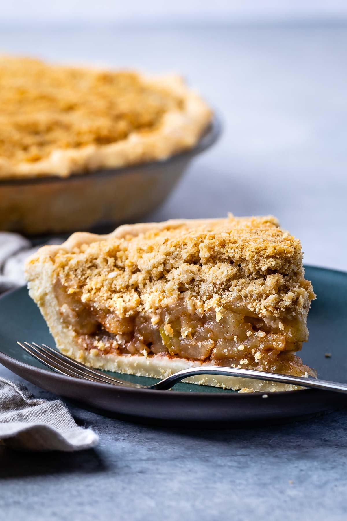 one slice of apple pie on a dark green plate with crumble topping