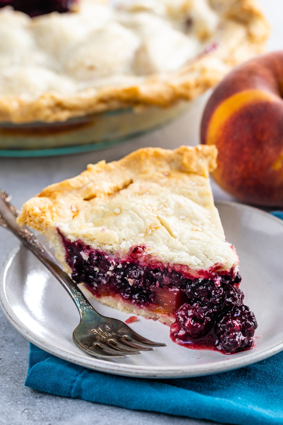 one slice of pie with blackberries pouring out the sides on a white plate