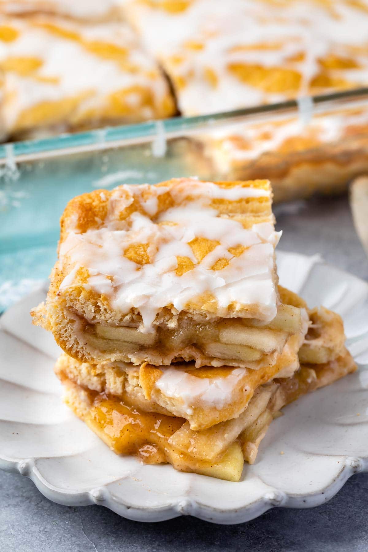 two slices of apple pie with frosting on top sitting on a light grey plate