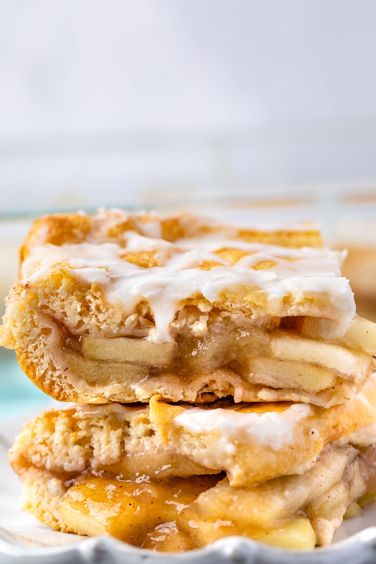 two slices of apple pie with frosting on top sitting on a light grey plate