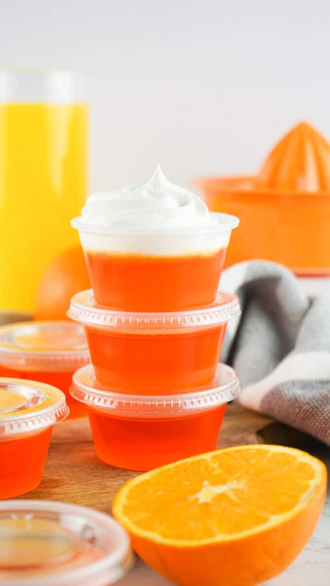 Three orange jello shots stacked on top of eachother with more around the bottom