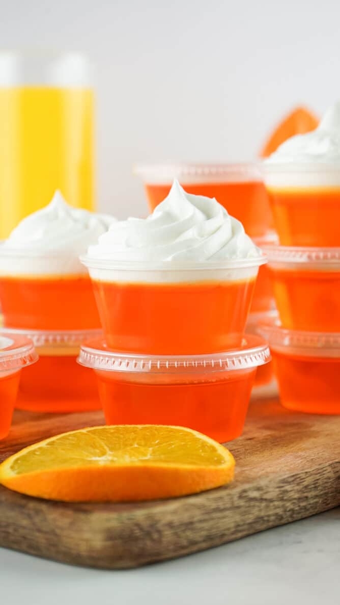 Orange creamsicle jello shots stacked on top of eachother and topped with whipped cream