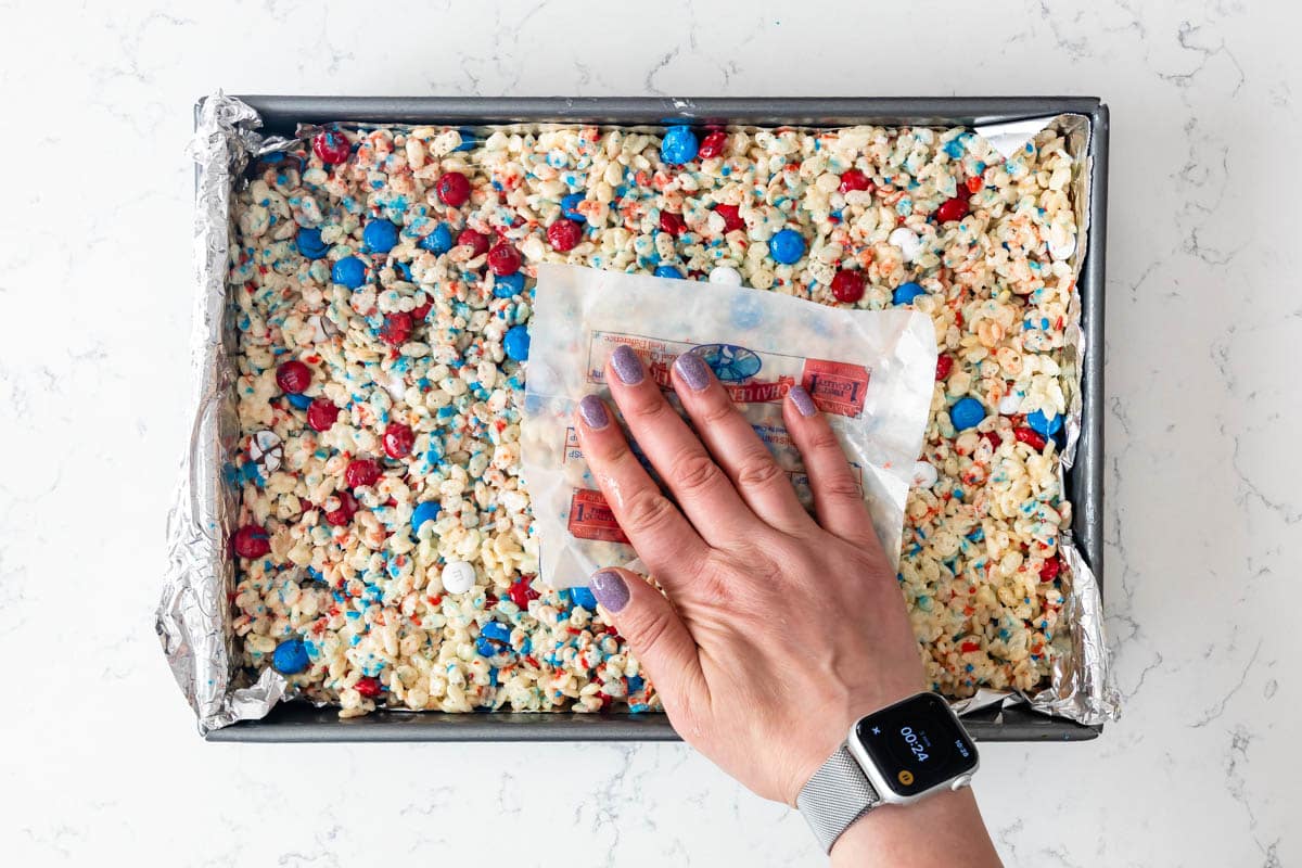 hand using butter wrapper to press rice krispie treats into pan.