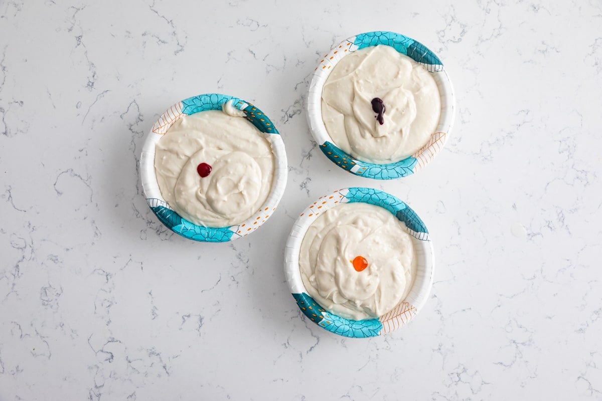 cake batter in 3 paper bowls with dots of food coloring