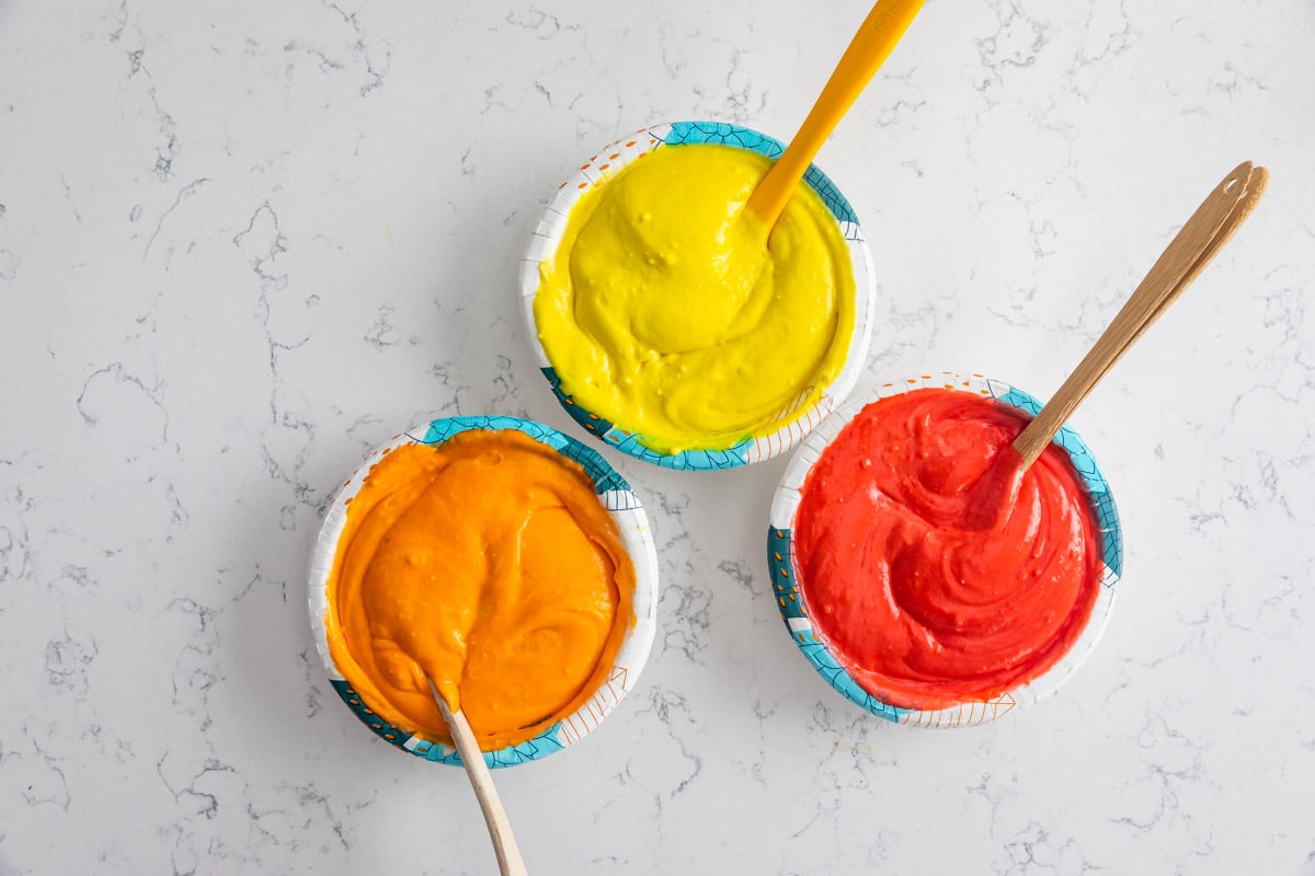 cake batter in 3 paper bowls with food coloring