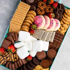 teal board with many types of cookies and marshmallows and strawberries sprinkled through out