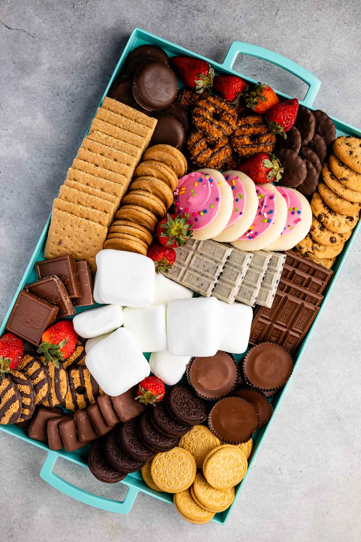 teal board with many types of cookies and marshmallows and strawberries sprinkled through out