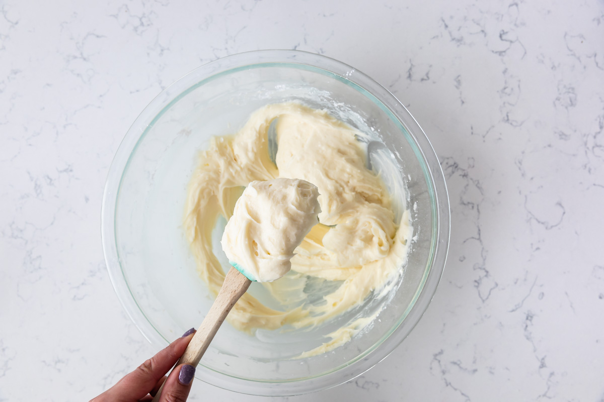 bowl of frosting with spatula being held by hand.