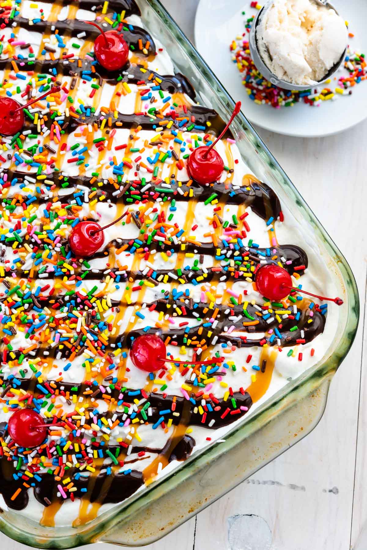 overhead shot of poke cake with frosting, chocolate sauce, and cherries on top in a clear pan