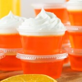 Orange creamsicle jello shots stacked on top of eachother and topped with whipped cream and recipe title on top