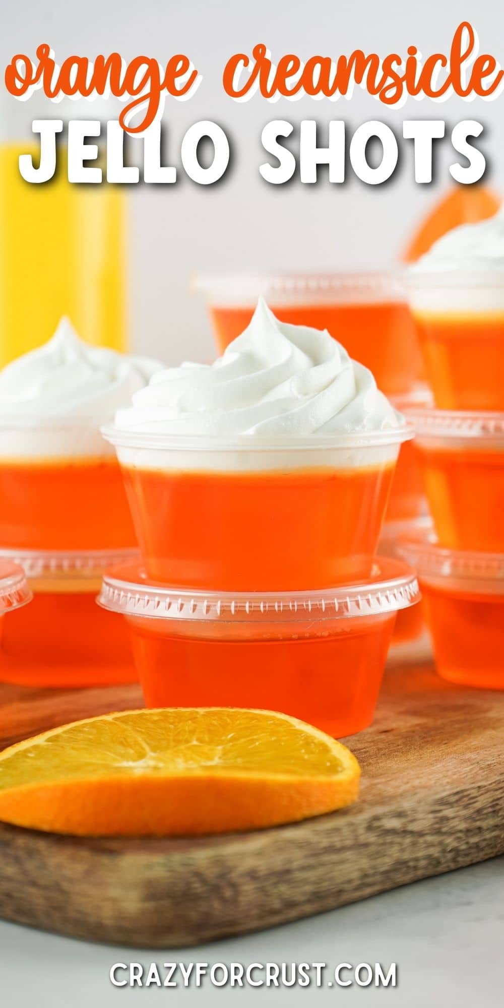 Orange creamsicle jello shots stacked on top of eachother and topped with whipped cream and recipe title on top