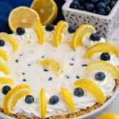 Side shot of lemon blueberry pie surrounded by blueberries and lemons