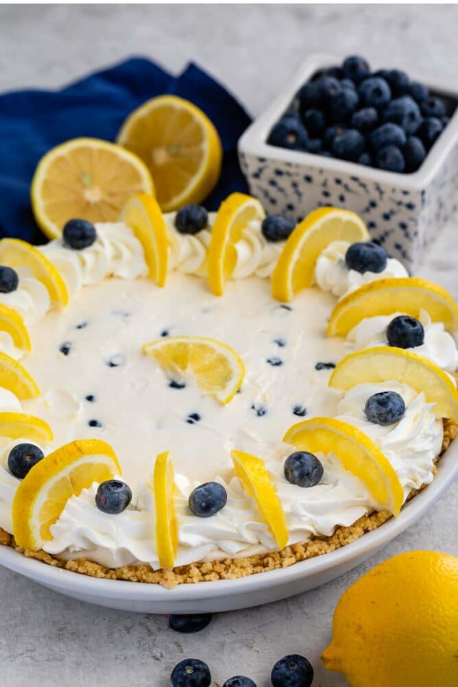 Side shot of lemon blueberry pie surrounded by blueberries and lemons