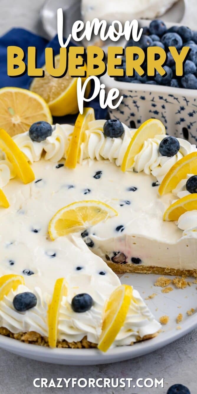 Lemon blueberry pie with one slice cut out of dish and blueberries and lemons in background and recipe title on top of photo