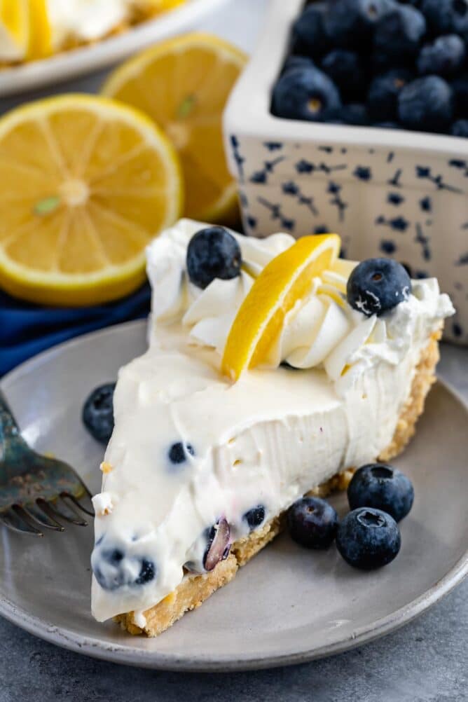 One slice of lemon blueberry pie on a plate topped with blueberries and a lemon slice