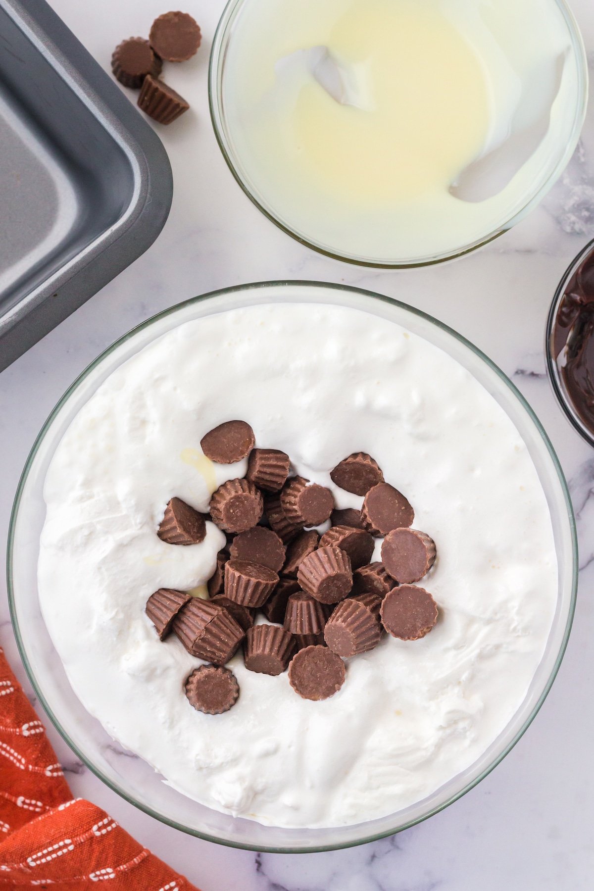 a clear bowl holding white ice cream with mini Reeses peanut butter cups ready to be mixed in