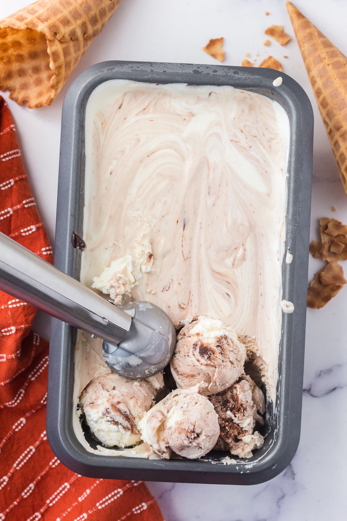 ice cream in a pan with an ice cream scoop scooping a couple balls of ice cream,