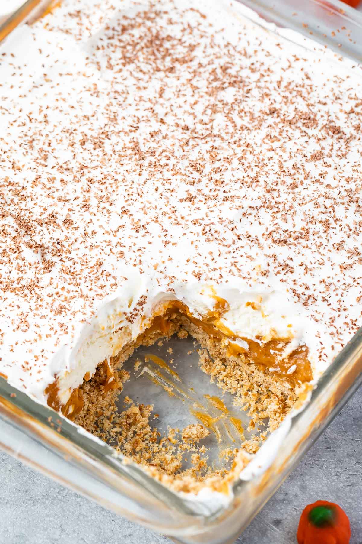 full clear pan of pumpkin dessert with white frosting and a slice taken out of the pan