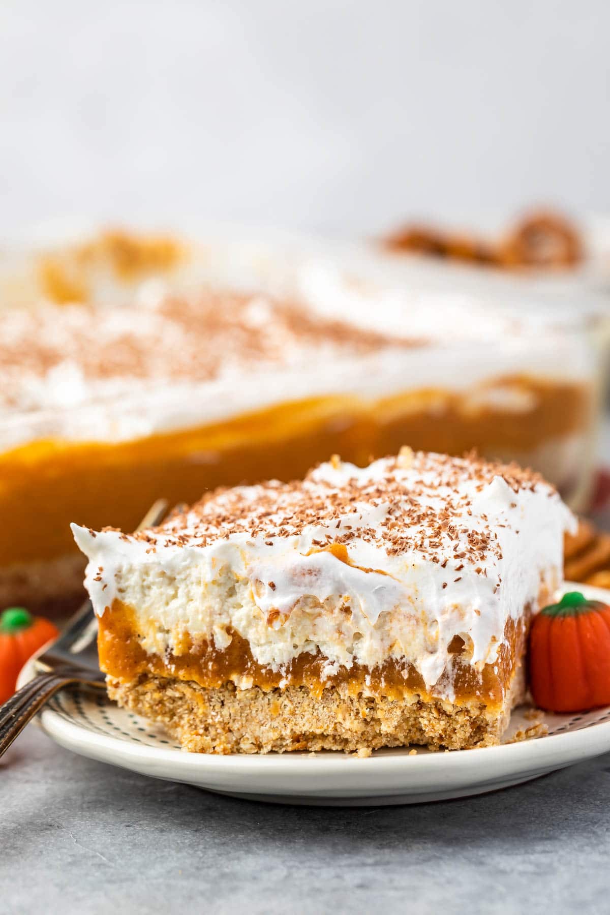 a slice pumpkin dessert sitting on a white plate with white frosting and pumpkin topping