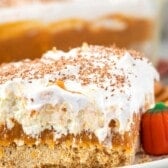 a slice pumpkin dessert sitting on a white plate with white frosting and pumpkin topping