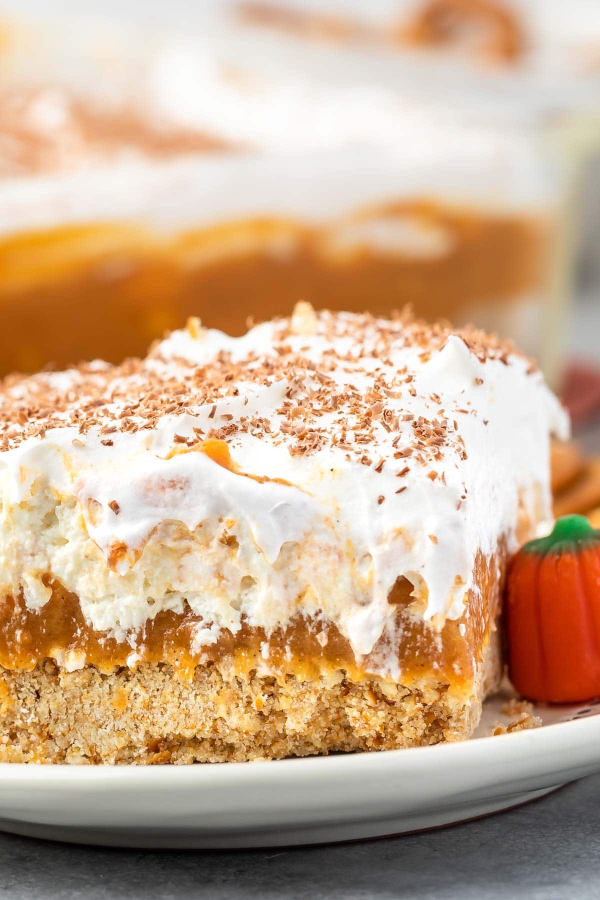 a slice pumpkin dessert sitting on a white plate with white frosting and pumpkin topping