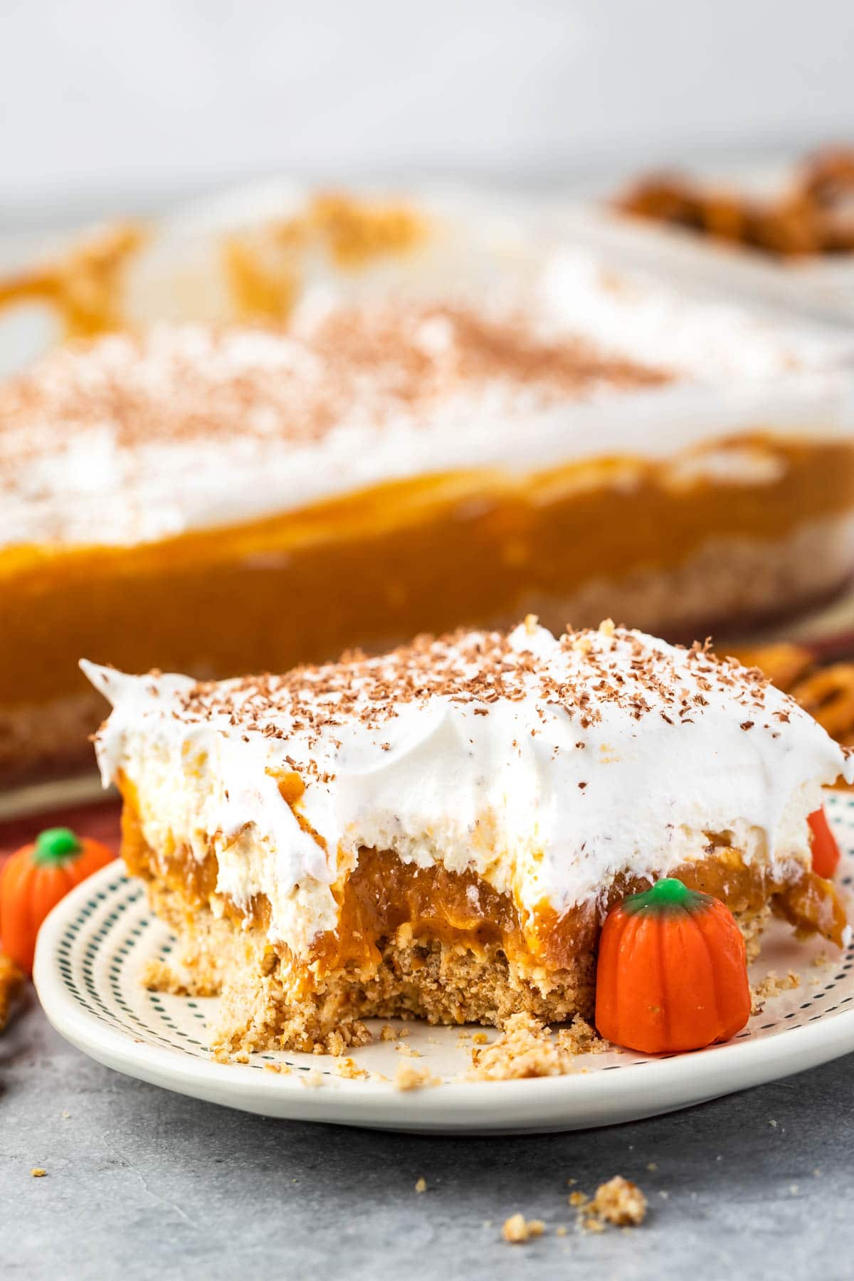 a slice pumpkin dessert sitting on a white plate with white frosting and pumpkin topping