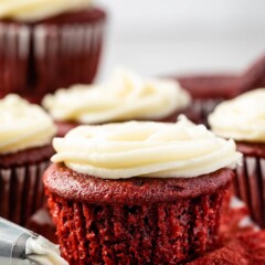 Red velvet cupcake topped with cream cheese frosting with more in background