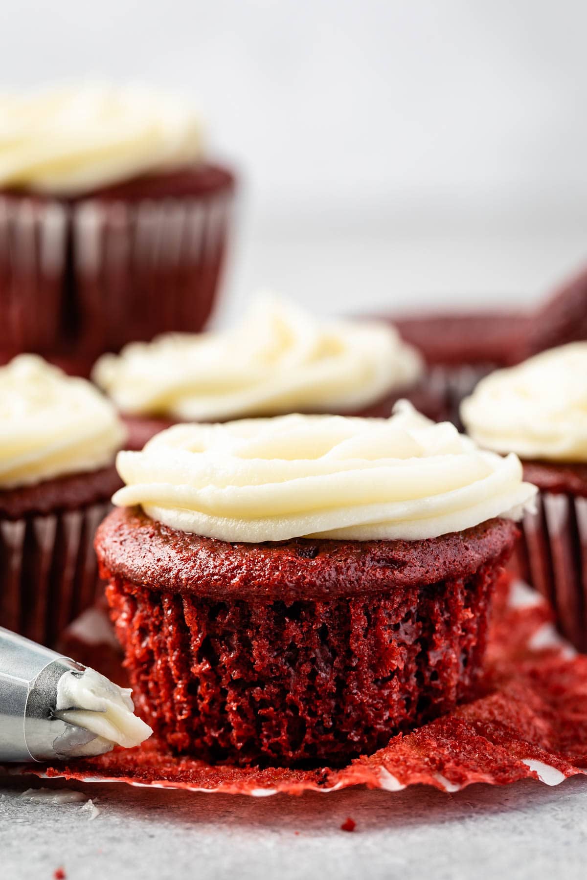 Red velvet cupcake topped with cream cheese frosting with more in background