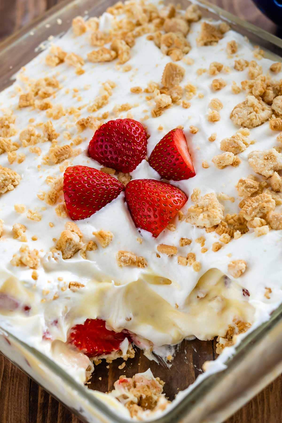 shortcake in a clear pan with four sliced strawberries in the center and a piece taken out of the corner