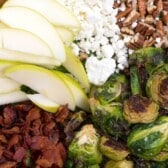 brussel sprout salad with all the ingredients including apples, Brussel sprouts, cheese, and bacon separated in a wooden bowl with words on the photo