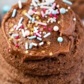 stacked chocolate cookies with the one on top frosted with colorful sprinkles with words on top