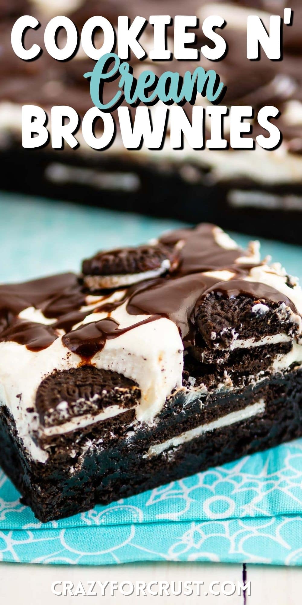 square slice of brownies with white frosting and chocolate drizzle on top sitting on a teal cloth with words on the photo