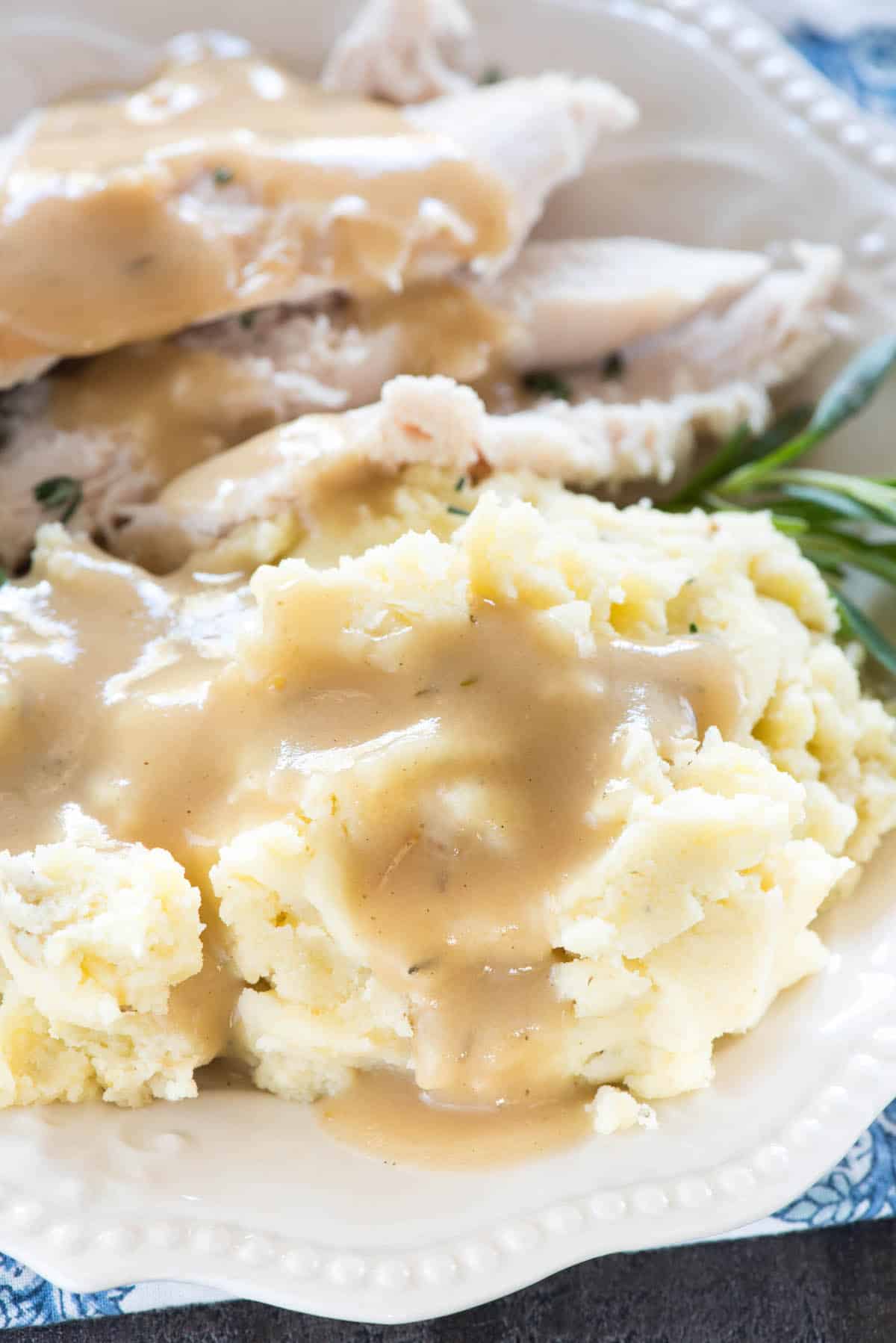 mashed potatoes on a white plate next to sliced turkey and covered in gravy