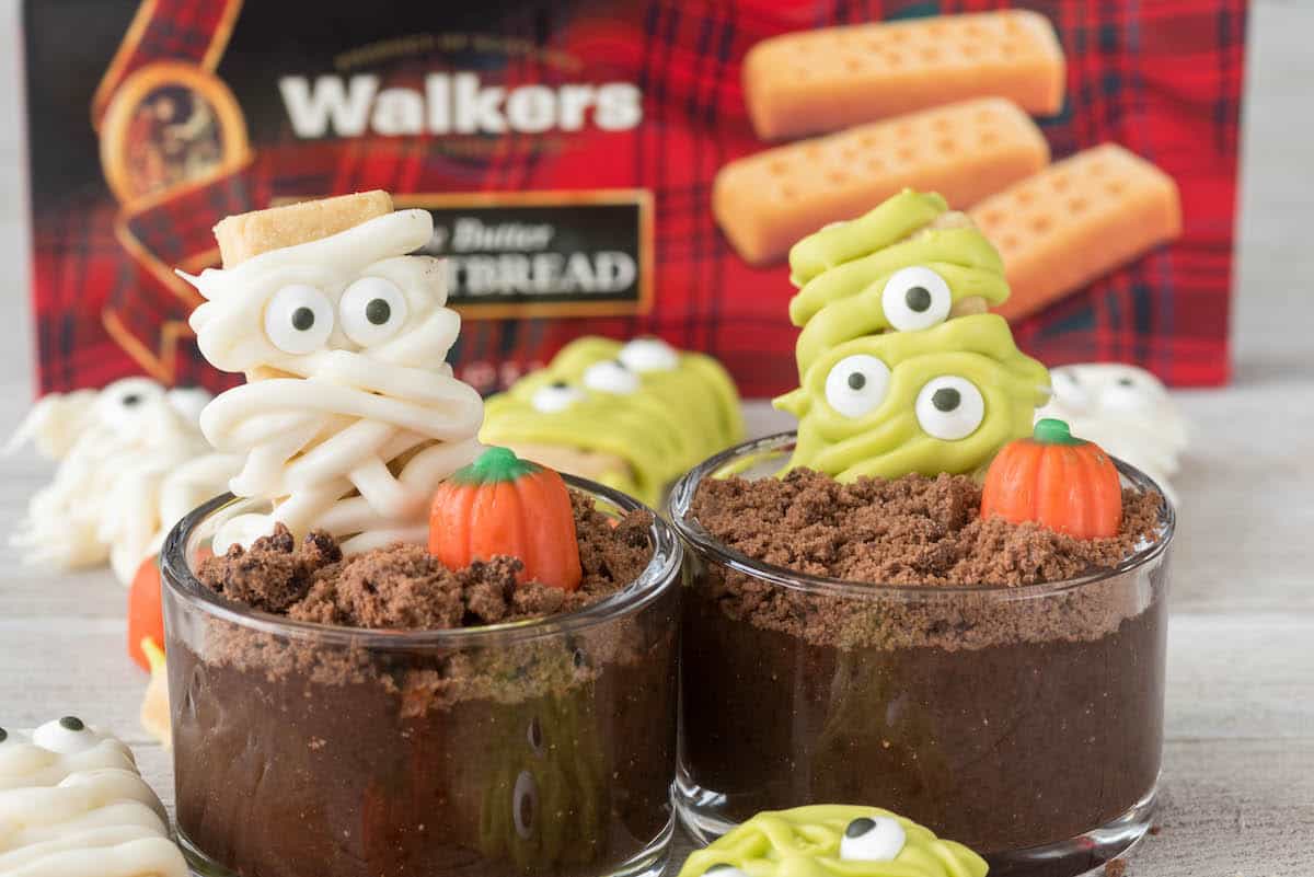mummy and monster decorated cookies in dirt cups next to a candy corn pumpkin