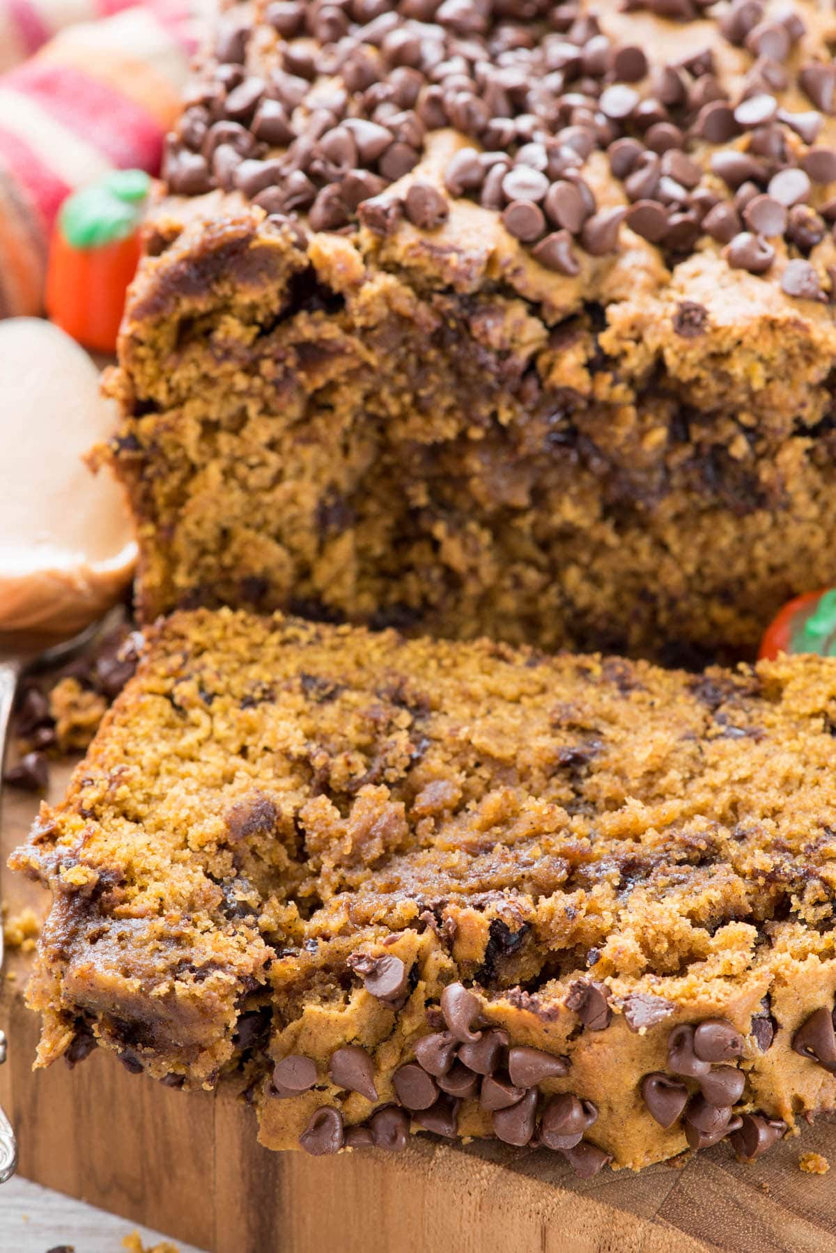 close up photo of loaf of pumpkin quick bread with chocolate chips, one slice laying on cutting board