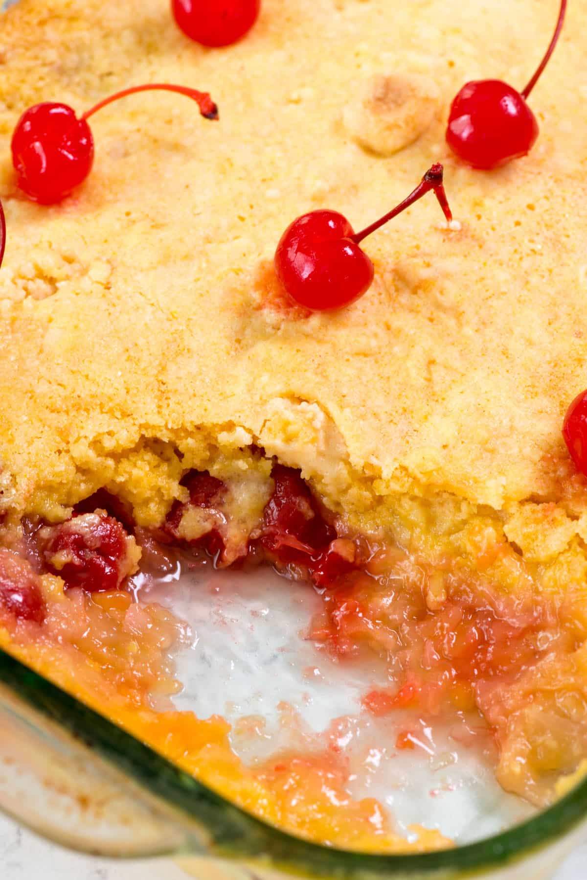 pineapple dump cake in glass pan with slice missing and cherries on top