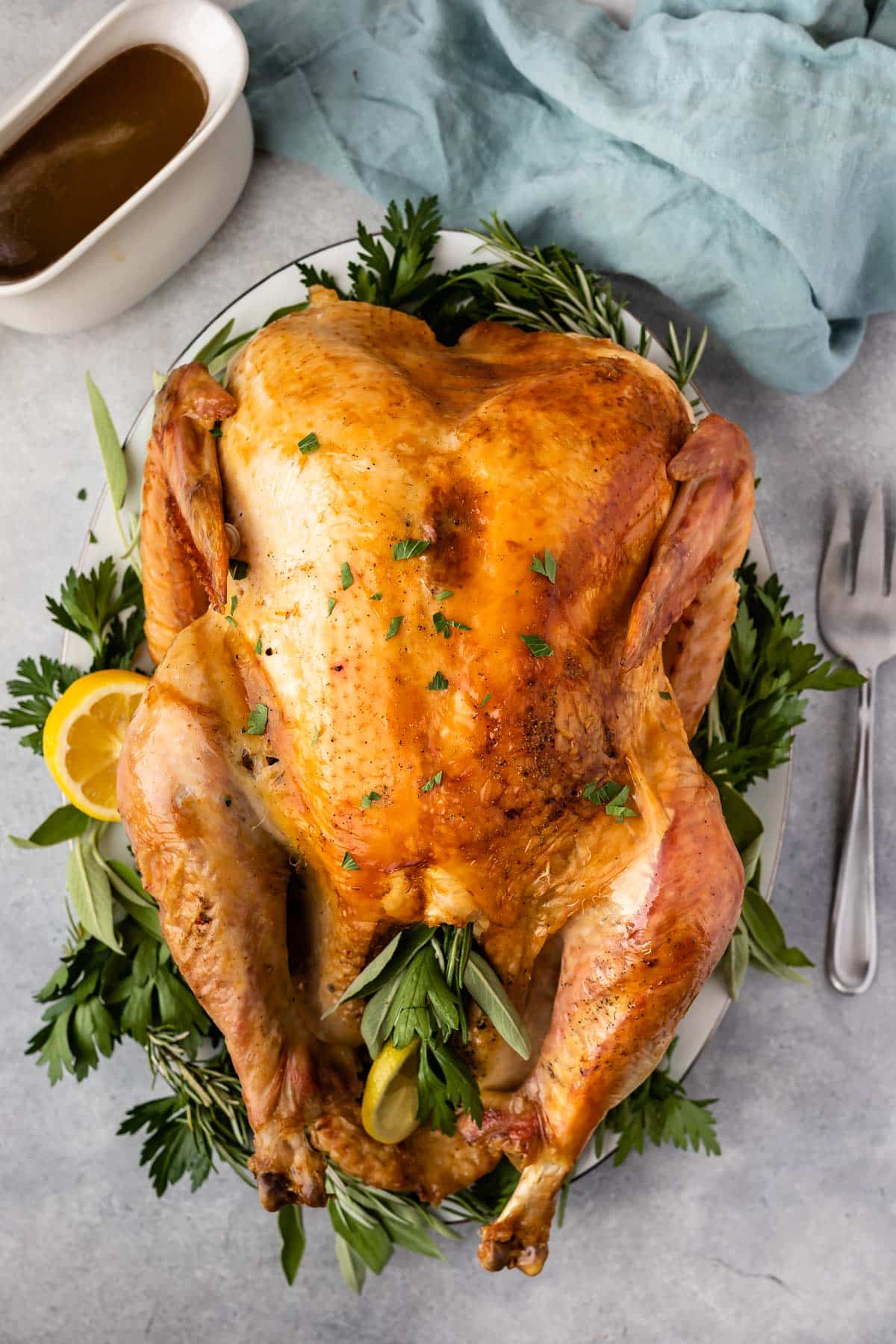 stuffed baked turkey surrounded by herbs on a white plate