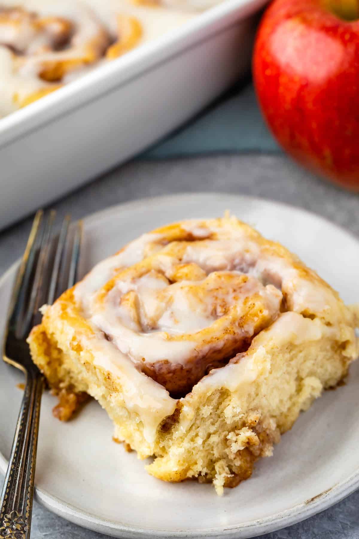 one cinnamon roll on a grey plate with a fork next to it