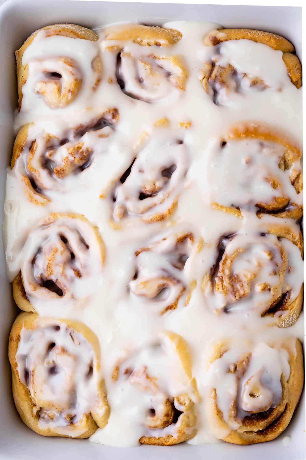 a white pan full of cinnamon rolls with icing on top