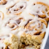 white pan of cinnamon rolls with one taken out