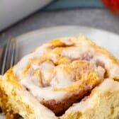 one cinnamon roll on a grey plate with a fork next to it with words on the top