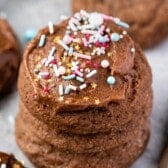 stacked chocolate cookies with the one on top frosted with colorful sprinkles