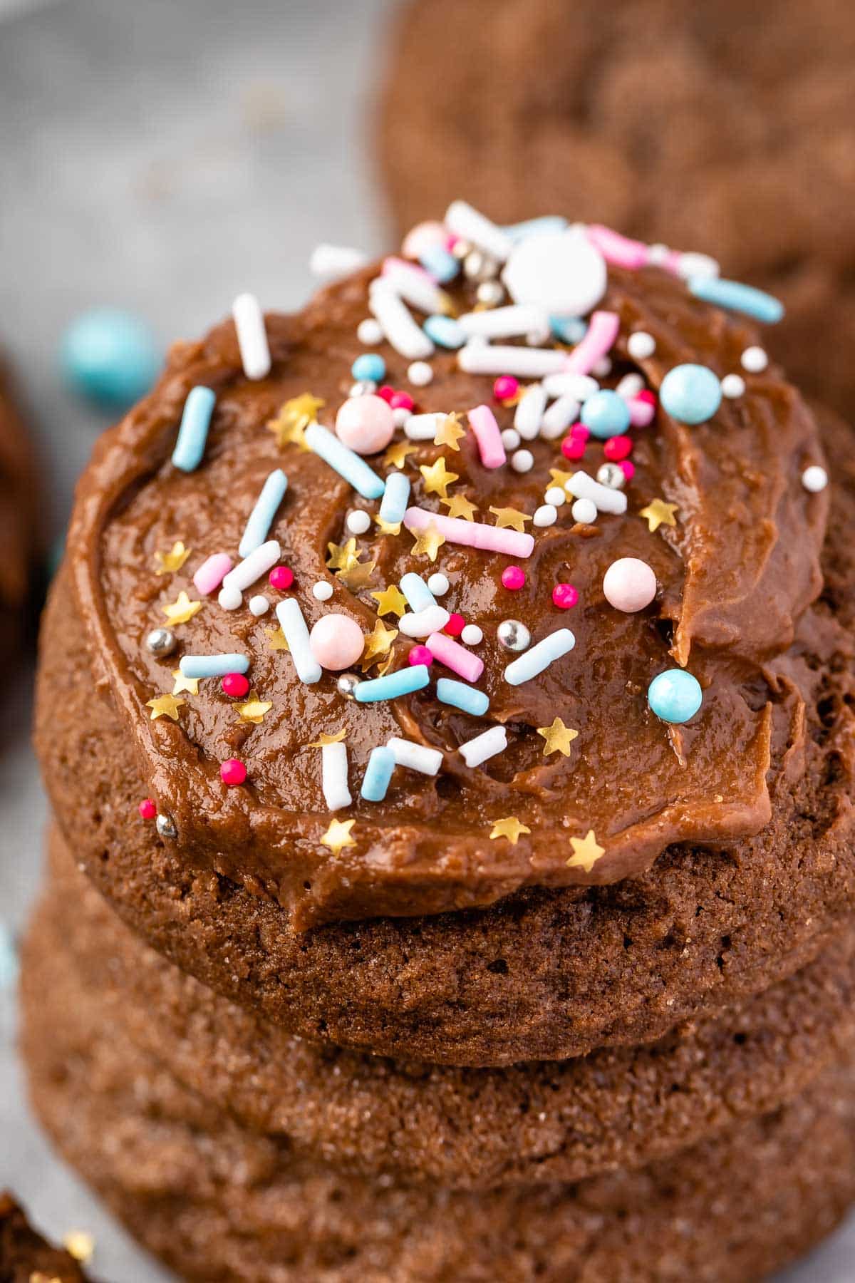 stacked chocolate cookies with the one on top frosted with colorful sprinkles