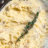 mashed potatoes in a black crockpot pan and herbs on top with words saying the name of the recipe