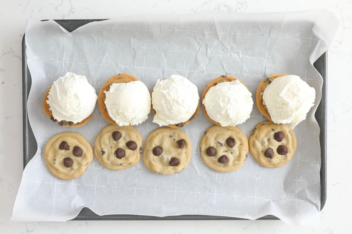 10 cookies on a parchment lined cookie sheet 5 face up and 5 face down with scoops of vanilla ice cream on top.