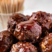 multiple meatballs stacked in a white bowl with words on top