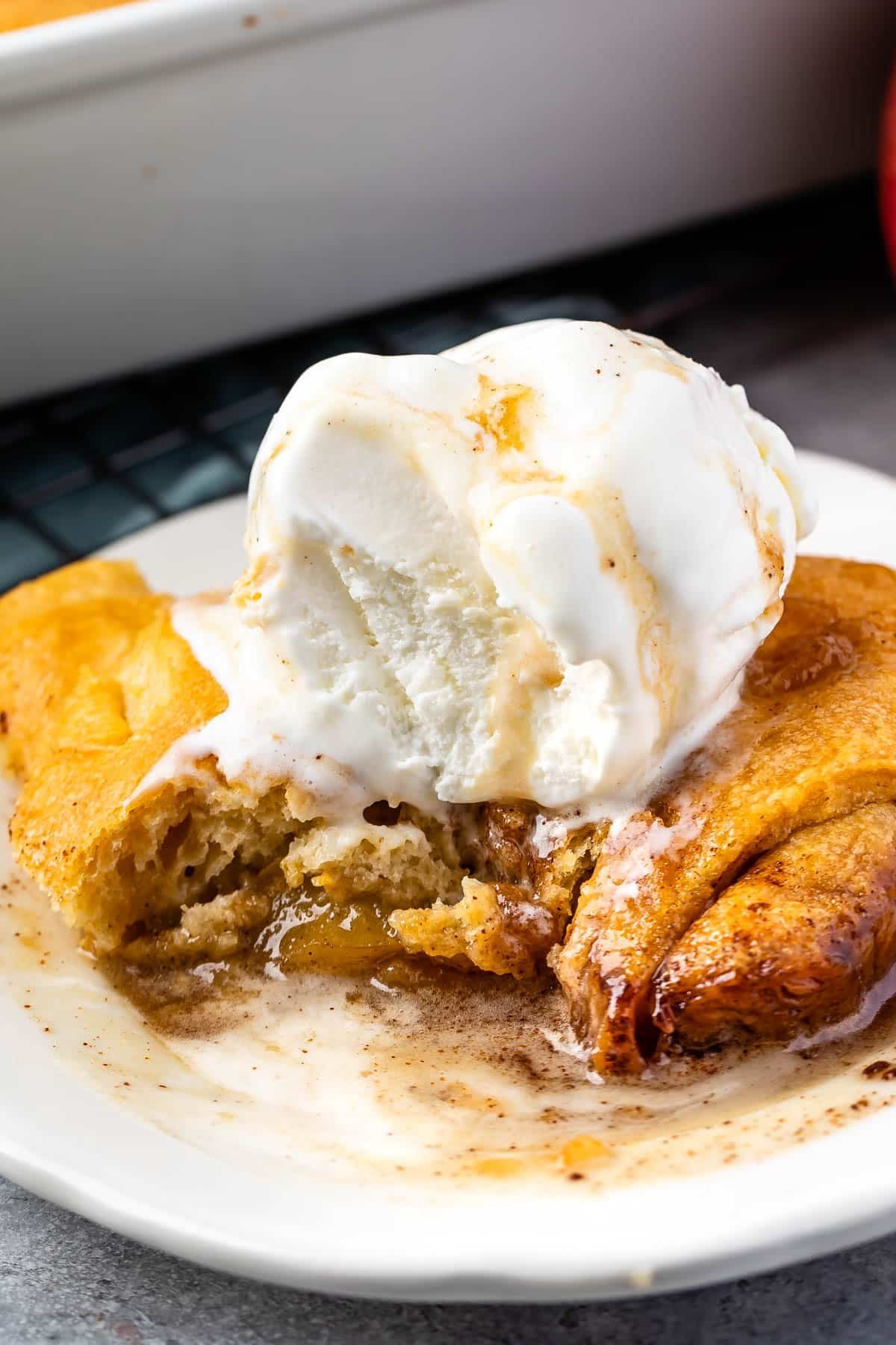 apple dumpling in a white plate with vanilla ice cream on top and a bite taken out of the dumpling