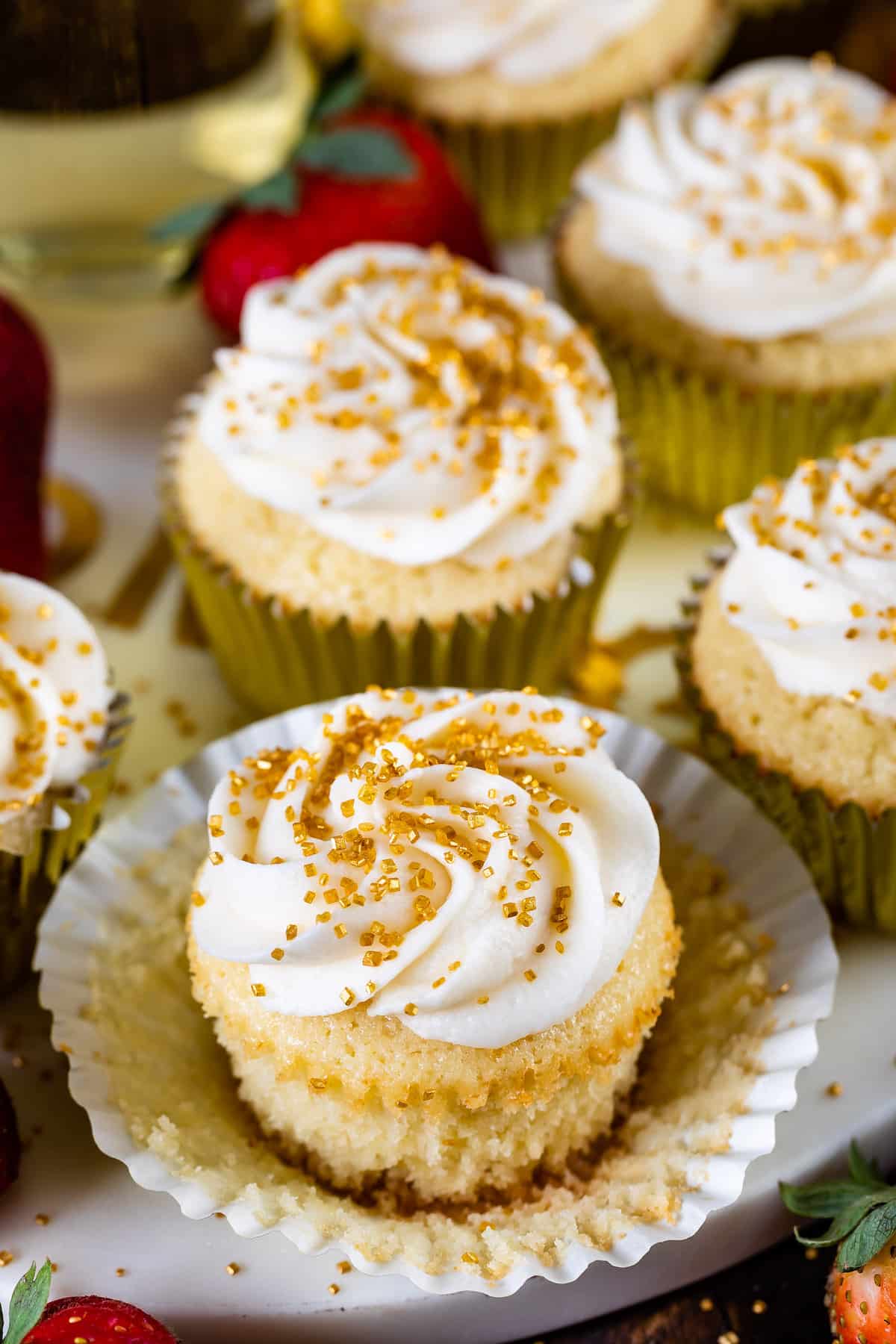 cupcakes in a gold tin with white frosting and gold sprinkles on top