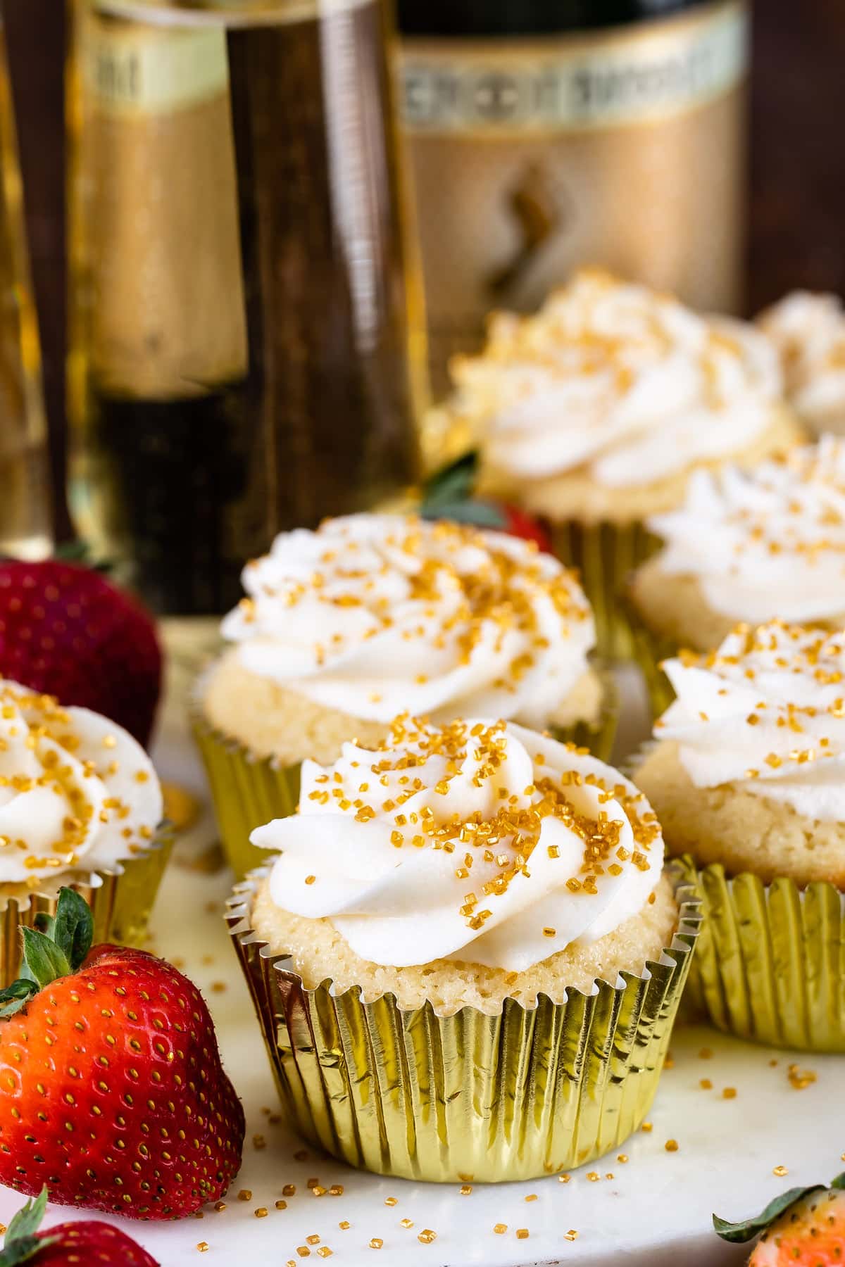 cupcakes in a gold tin with white frosting and gold sprinkles on top